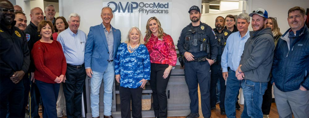 Mayor Moore's visit: a group of guests and OMP staff standing in the clinic lobby in front of the OMP OccMed Physicians sign